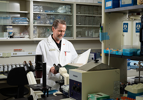 man in white lab coat in a lab staring at paperwork smiling