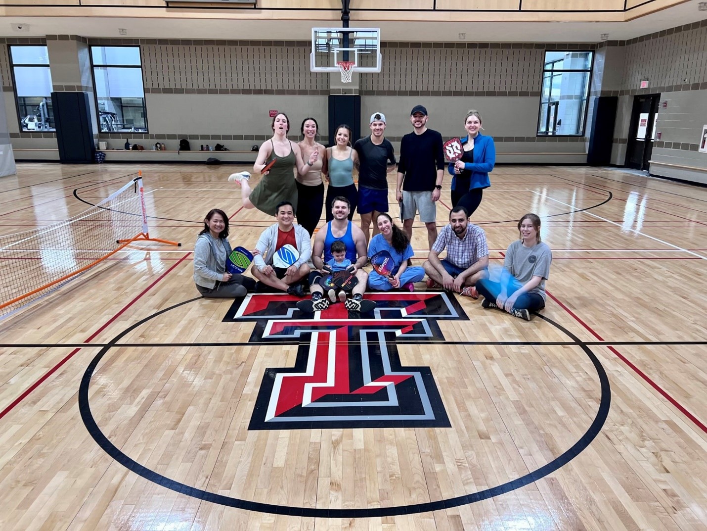 Surgery residents sitting on Texas Tech Pickleball court smiling holding paddles Surgery residents sitting on Texas Tech Pickleball court smiling holding paddles